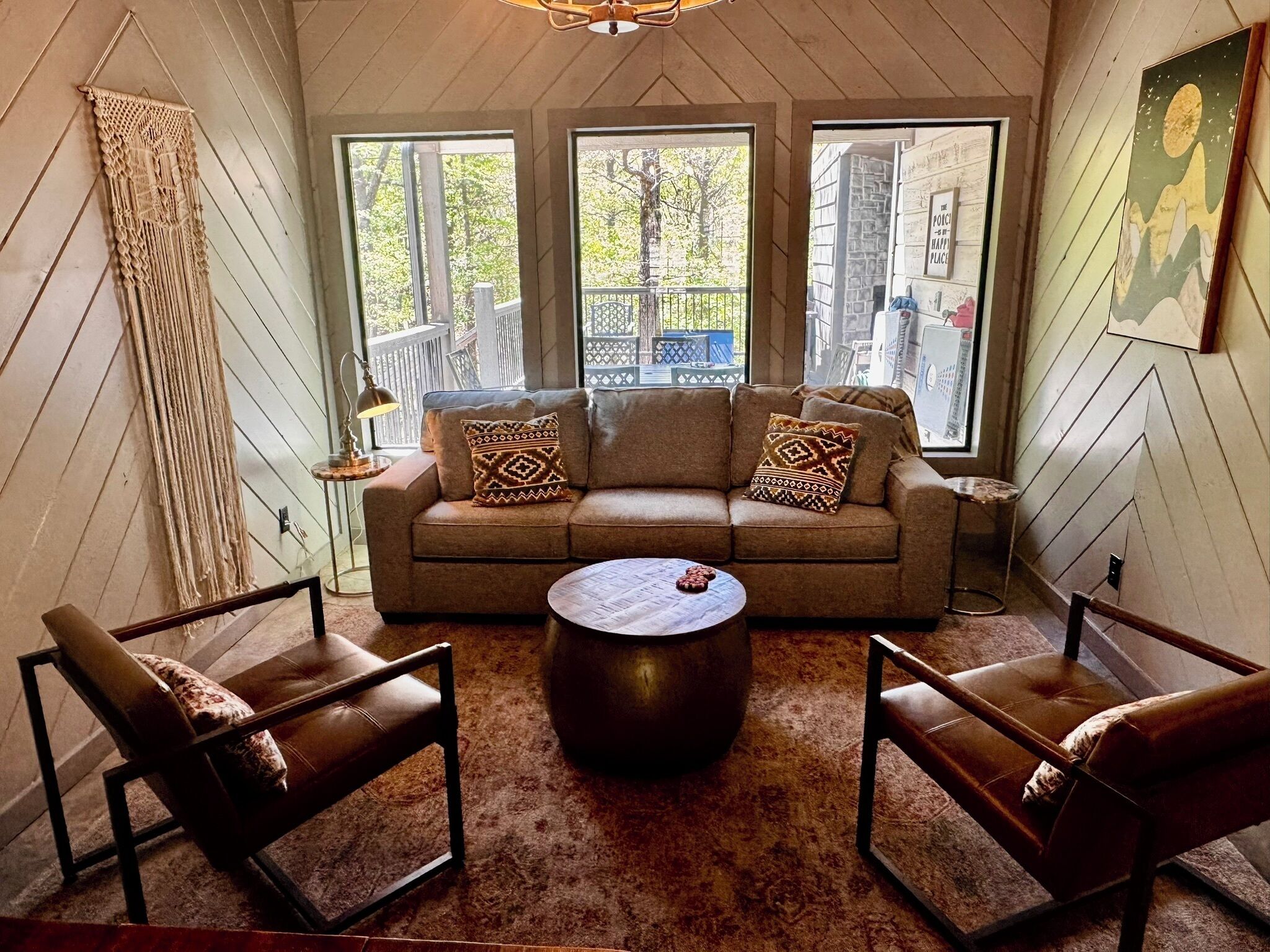 A cozy room with a sofa, two chairs, a coffee table, and large windows offering a view of the outside.