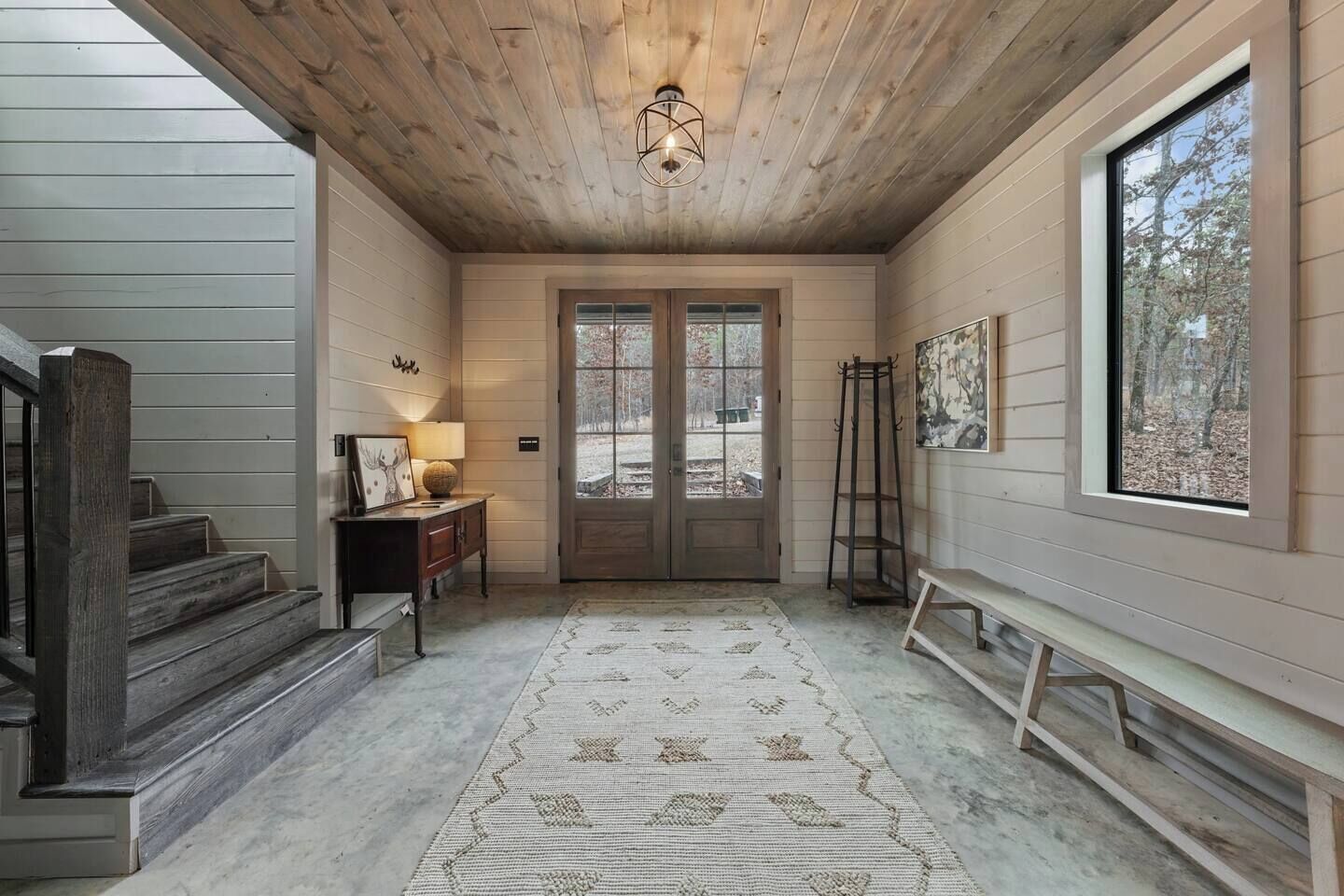 A wooden interior with a staircase, a rug, a bench, a door, and a window.