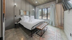 Une chambre à coucher avec un grand lit, un banc, une table de chevet, un miroir et une fenêtre avec des rideaux.