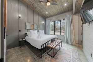 Ein Schlafzimmer mit einem großen Bett, einer Bank, einem Nachttisch, einem Spiegel und einem Fenster mit Vorhängen.