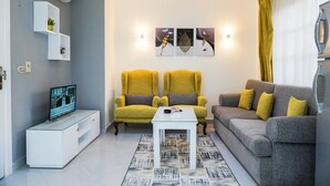 Ein modernes Wohnzimmer mit Fernseher, zwei gelben Sessel, einem grauen Sofa und einem weißen Couchtisch.