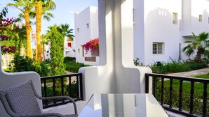 Ein Balkon mit Korbstühlen und einem Glastisch, umgeben von weißen Gebäuden und viel Grün.