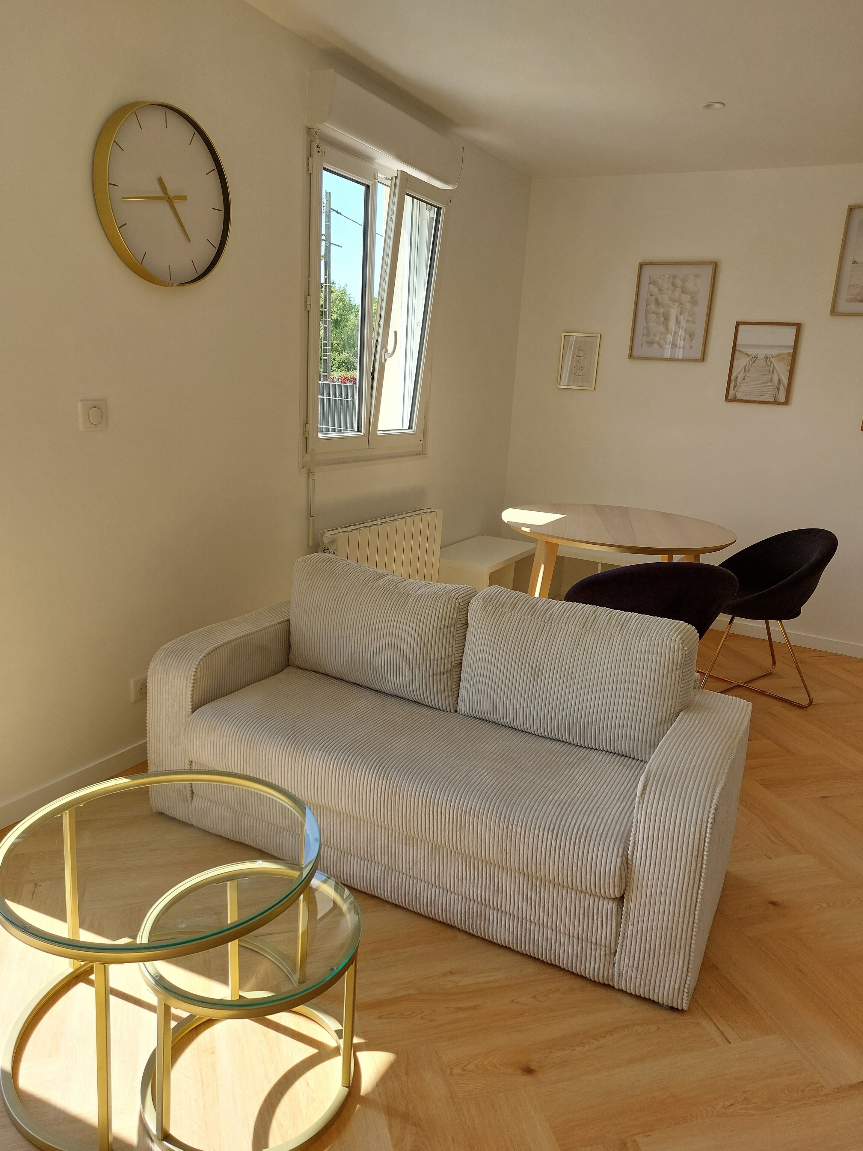 Ein Wohnzimmer mit einer Couch, einem Glastisch, einem Esstisch mit Stühlen und einer Wanduhr.