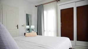 Une chambre d’hôtel avec un grand lit, une armoire en bois, une table de chevet avec une lampe et une fenêtre avec des rideaux.