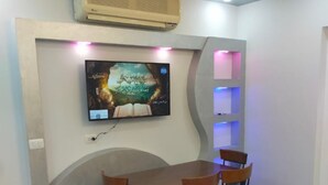 Zona pranzo con tavolo e sedie, una TV a parete e un condizionatore.