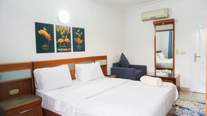 Hotelkamer met een houten bed, wit beddengoed, een blauwe fauteuil, een spiegel en drie kunstwerken aan de muur.