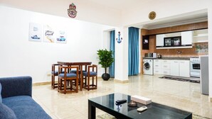 Een moderne woonkamer met een bank, een eettafel met stoelen, een salontafel, en een keuken met apparatuur en kasten.