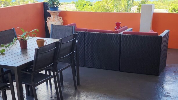 An outdoor patio with a table and chairs, a wicker sofa, and a view of the ocean.