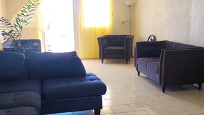 A living room with a sectional sofa, a dark armchair, and a purple sofa. There is a ceiling fan, a floor lamp, and a potted plant.