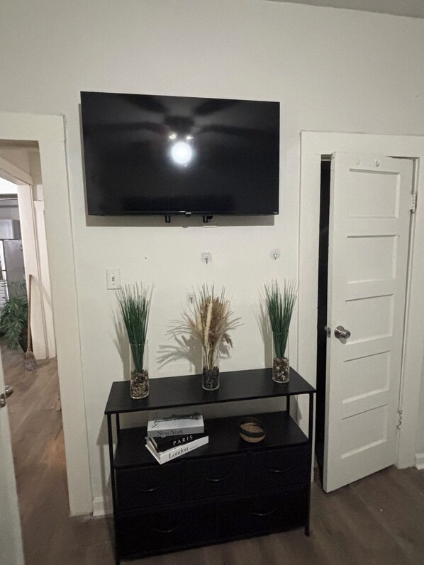 A living room with a flat-screen TV mounted on the wall, a black entertainment center with decorative plants, and a white door. - Westside Family home and small dog friendly in Atlanta. (Atlanta)