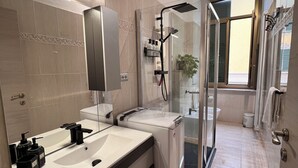 Et moderne badeværelse med to håndvaske, en glasbrusekabine og et synligt toilet.