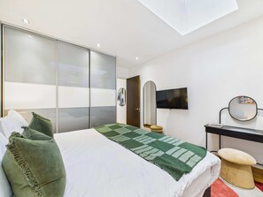 Ein modernes Schlafzimmer mit Bett, Schreibtisch, Stuhl, Fernseher und Kleiderschrank.