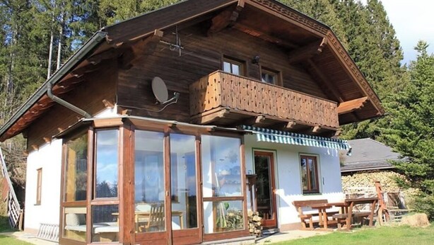 Un chalet en bois doté d’un balcon, de grandes fenêtres et d’une terrasse.