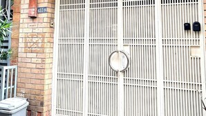 Una entrada protegida con un portón metálico, un balcón con techo de tejas y un muro de ladrillo.