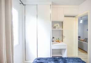 Ein Schlafzimmer mit einem Bett, einem Kleiderschrank, einem Schreibtisch mit Lampe und einem kleinen Regal mit Dekoration.