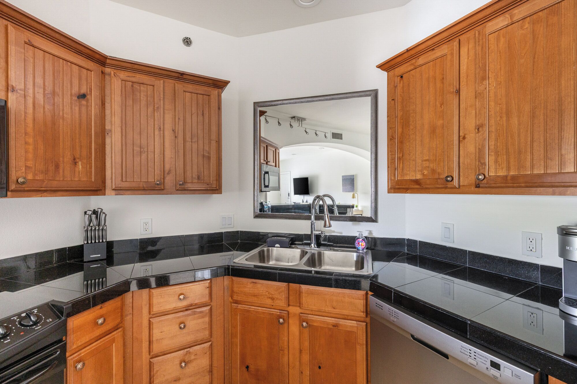 A kitchen with wooden cabinets, a black countertop, a stainless steel sink, and a dishwasher.