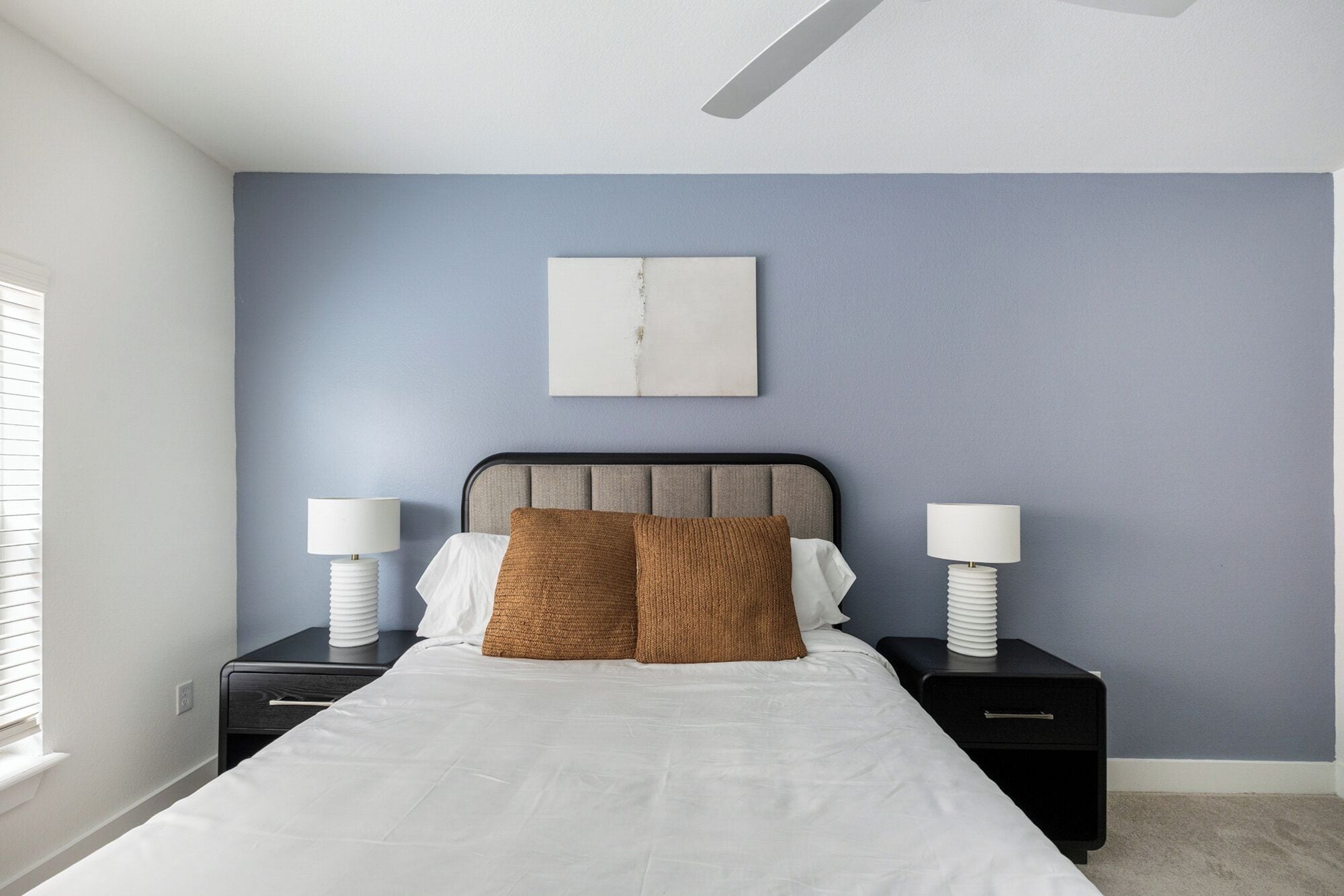 A bedroom with a bed, two bedside tables, a ceiling fan, and a wall-mounted artwork.