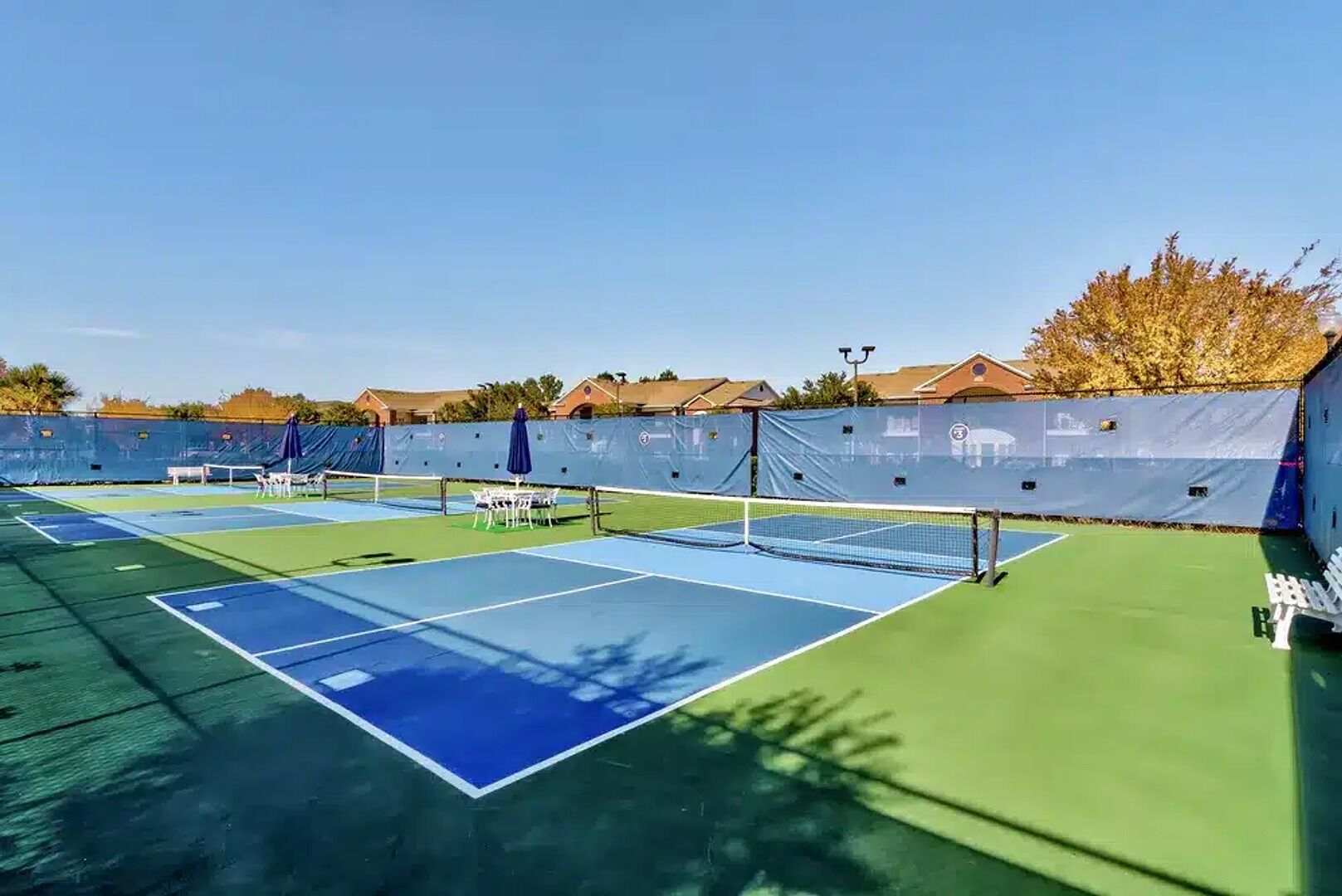 En udendørs tennisbane med flere baner, net og siddepladser.