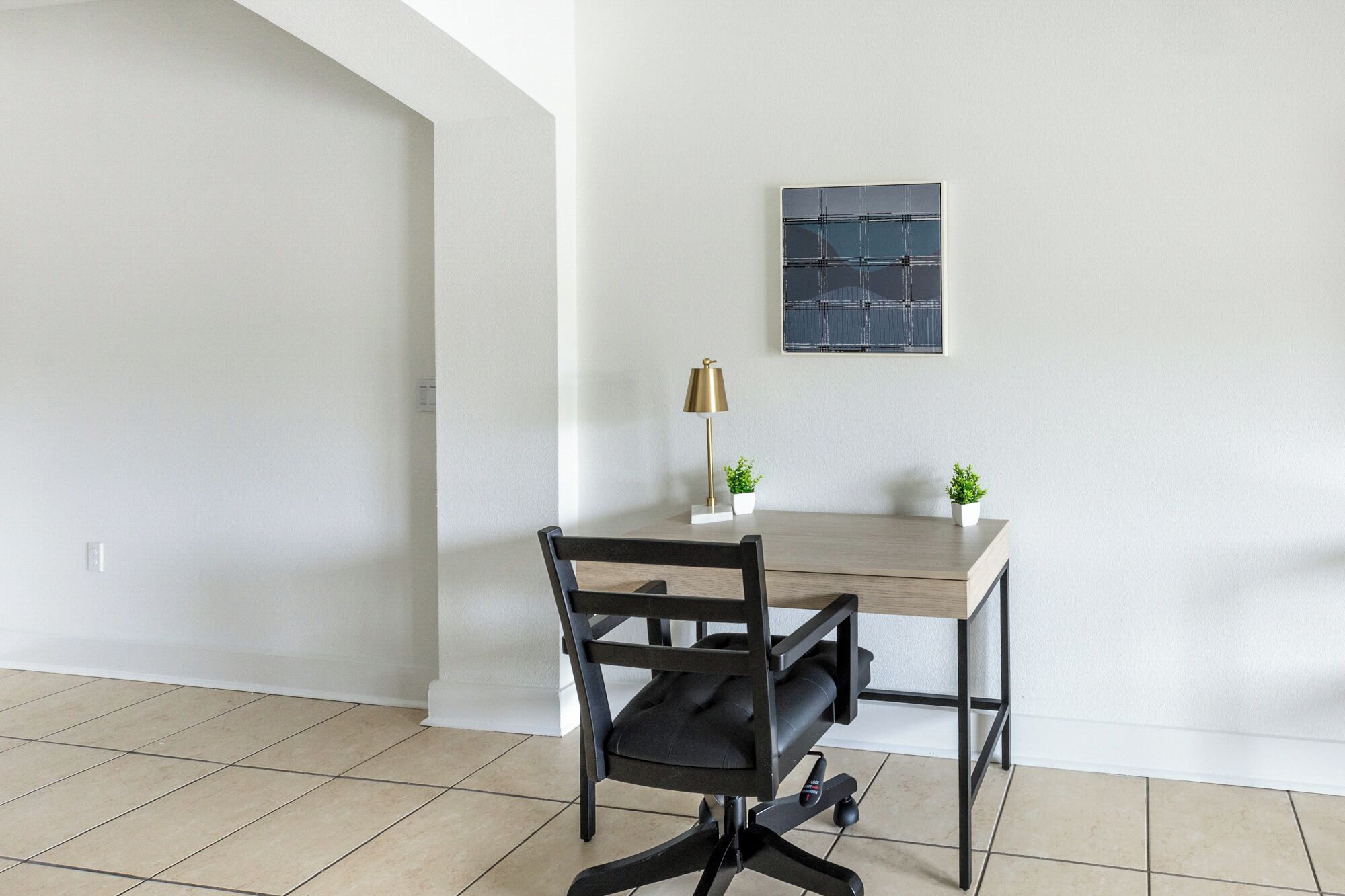 A modern office space with a wooden desk, black office chair, and a small potted plant.