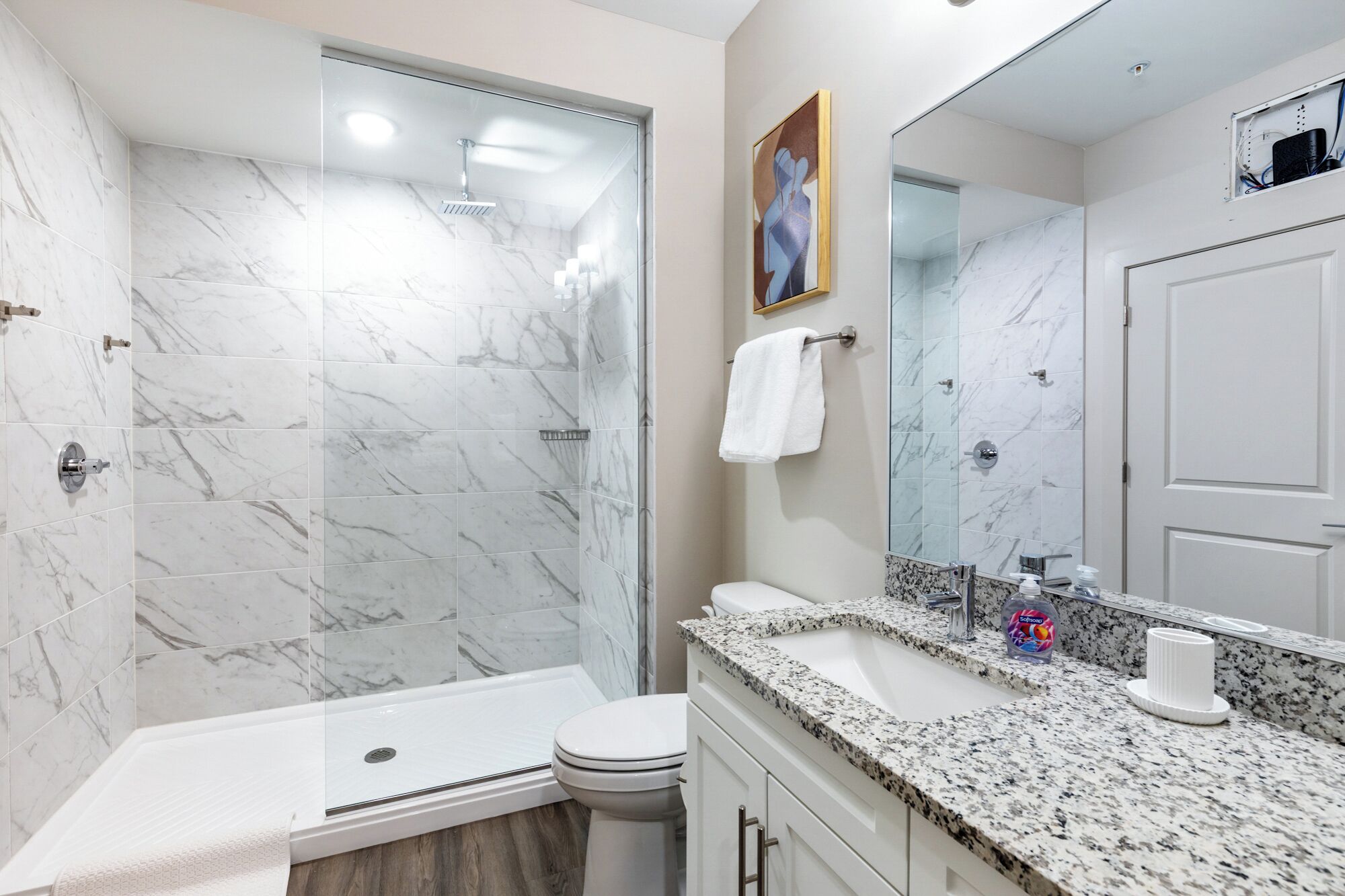 A modern bathroom with a glass-enclosed shower, a white toilet, and a granite countertop with a sink and soap dispenser.