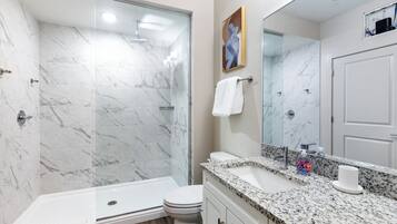A modern bathroom with a glass-enclosed shower, a white toilet, and a granite countertop with a sink and soap dispenser.