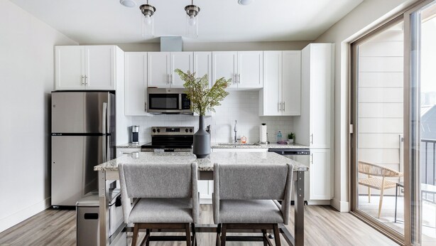 A modern kitchen with white cabinets, stainless steel appliances, and a central island with two grey chairs. - Landing Apartments near Rivergate Park Area (Cleveland)