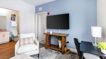 Una sala de estar moderna con un televisor de pantalla plana montado en la pared, un sofá blanco, una mesa de centro de madera y una mesa de comedor con sillas.
