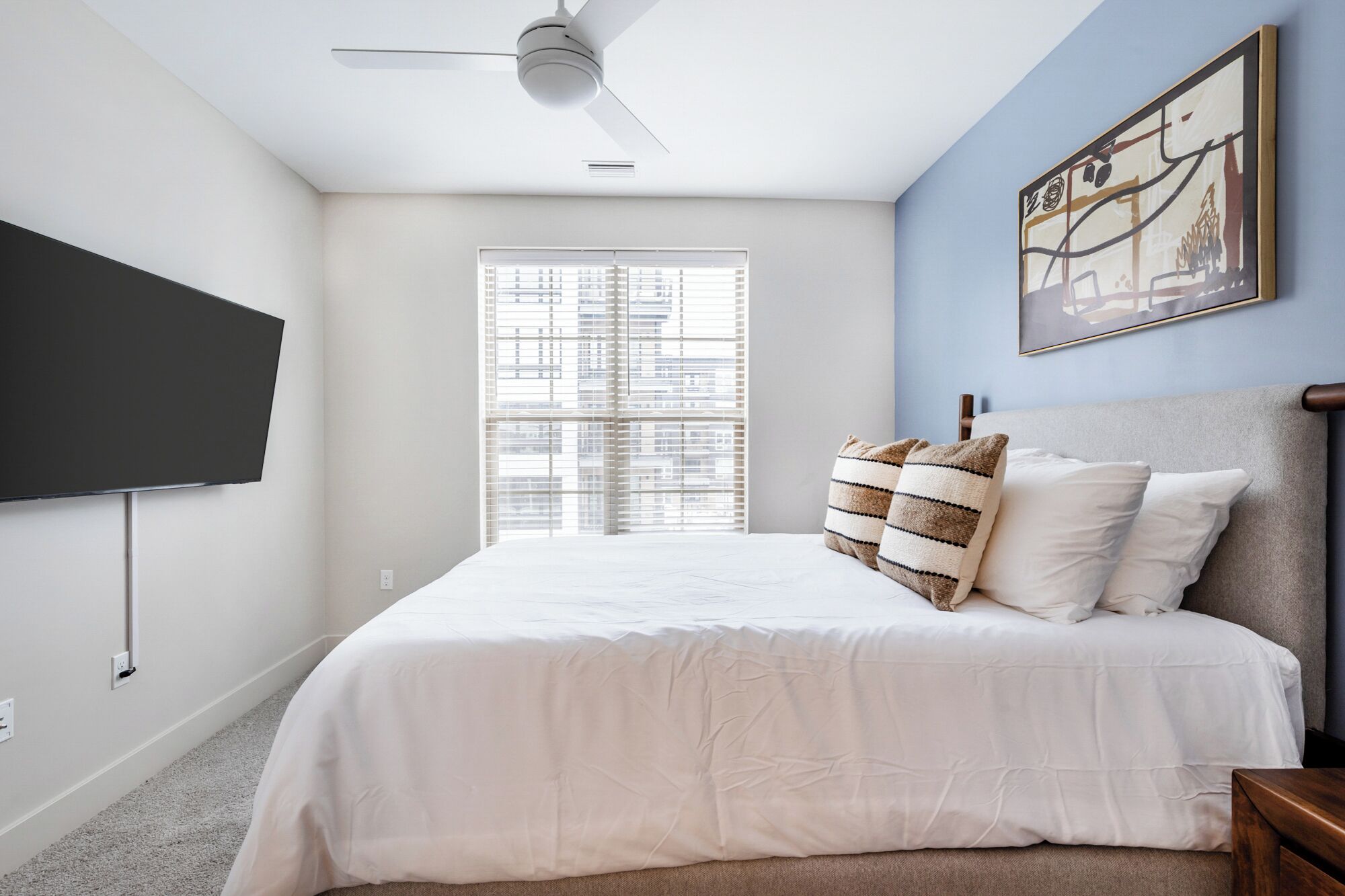 A bedroom with a bed, a ceiling fan, a window with blinds, and a painting on the wall.
