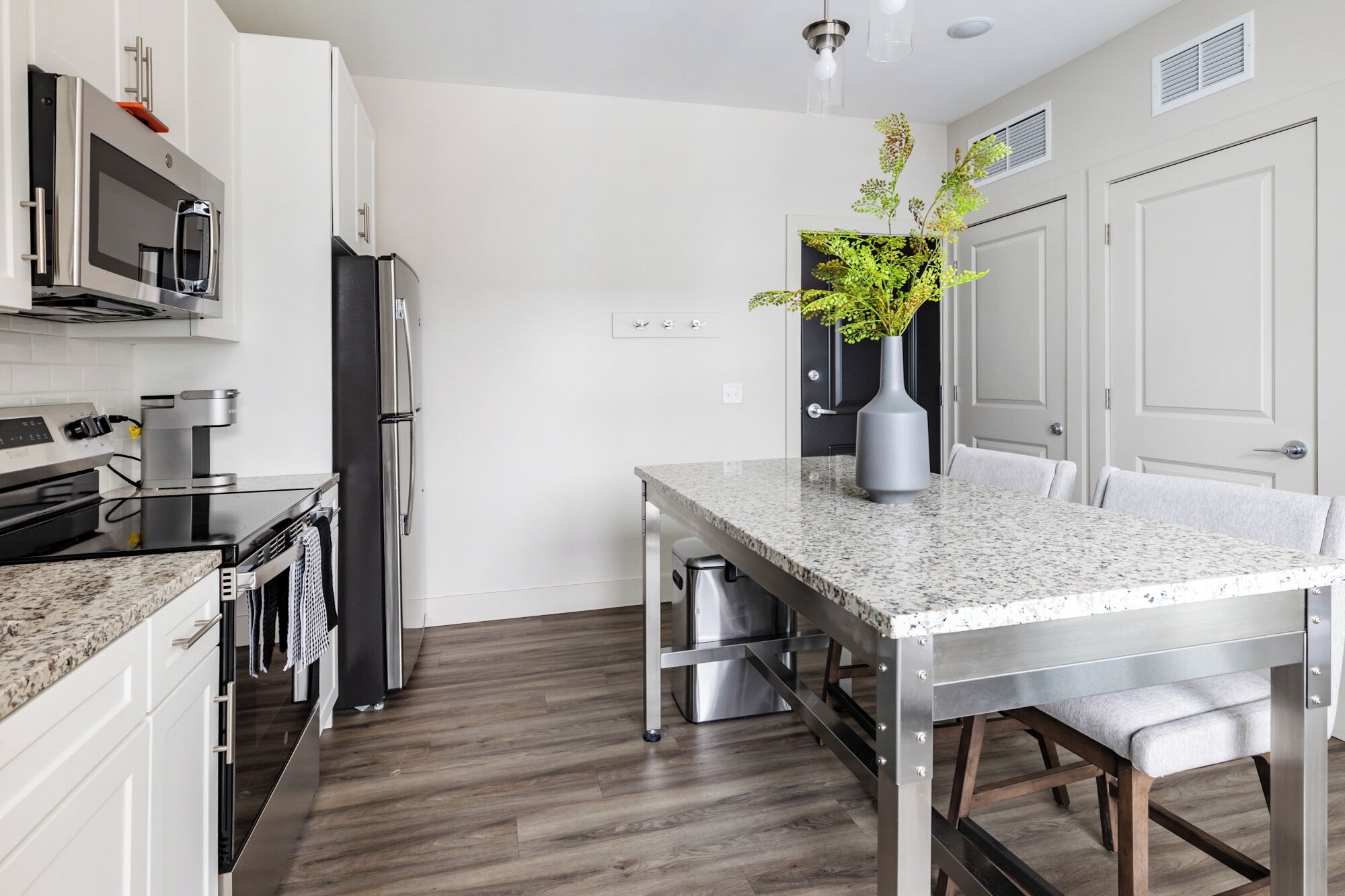 A modern kitchen with a granite countertop, stainless steel appliances, and a dining area with a bench.