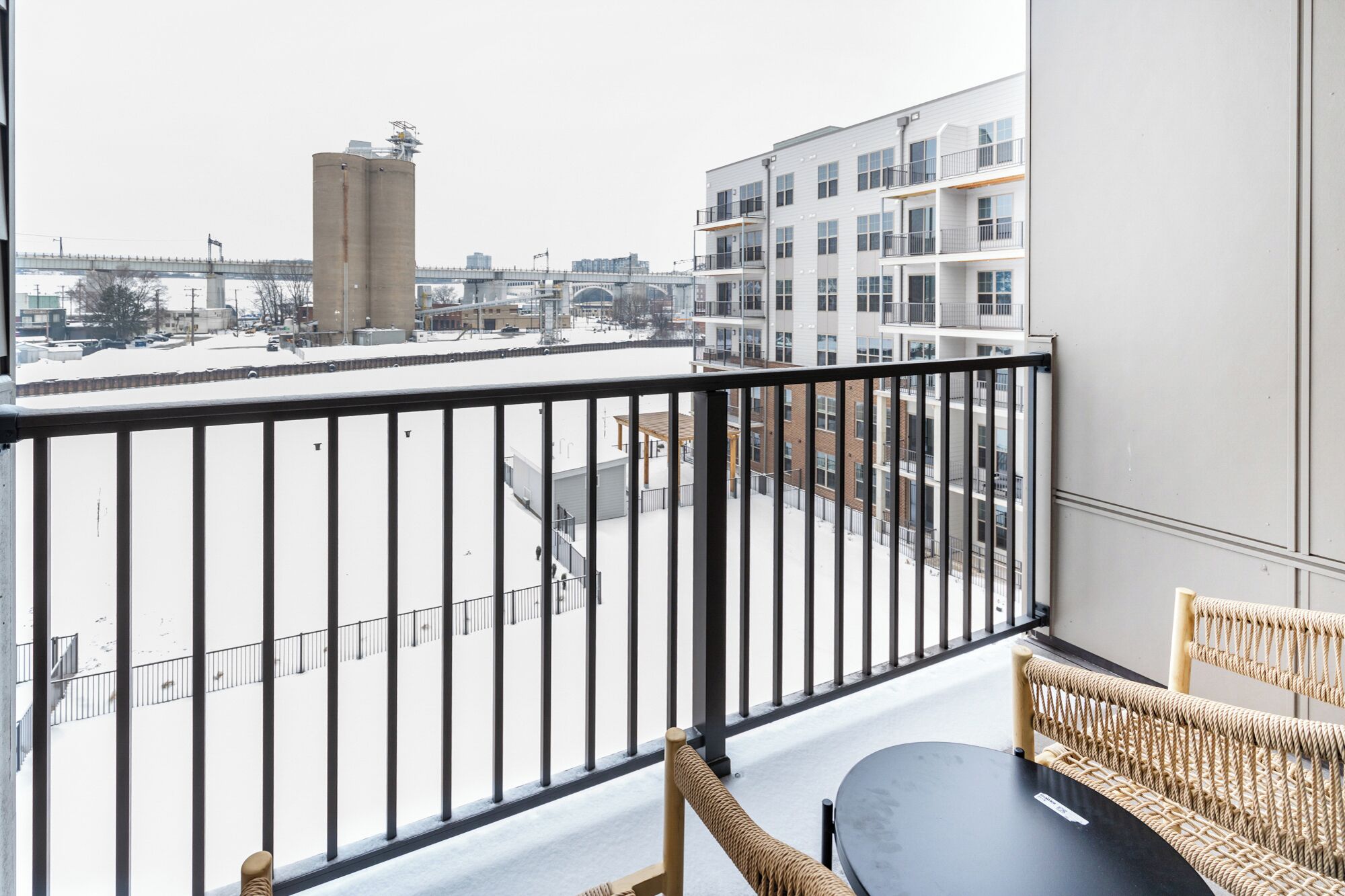 Ein Balkon mit Blick auf ein verschneites Stadtgebiet, eine hohe zylindrische Struktur und ein mehrstöckiges Gebäude mit Balkonen.