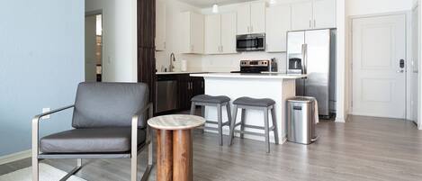 A modern kitchen with a central island, stainless steel appliances, and a grey leather chair.