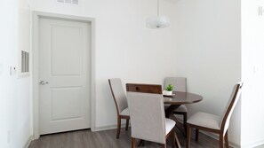 Un coin repas avec une table ronde, quatre chaises, une petite plante en pot et une porte blanche.