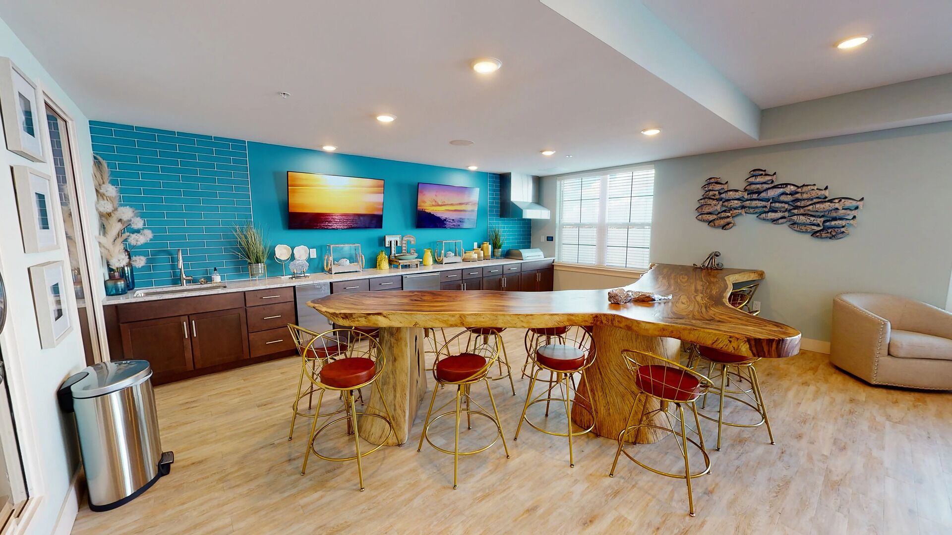 A modern kitchen with a wooden bar and red bar stools, a blue tiled backsplash, and artwork on the walls.