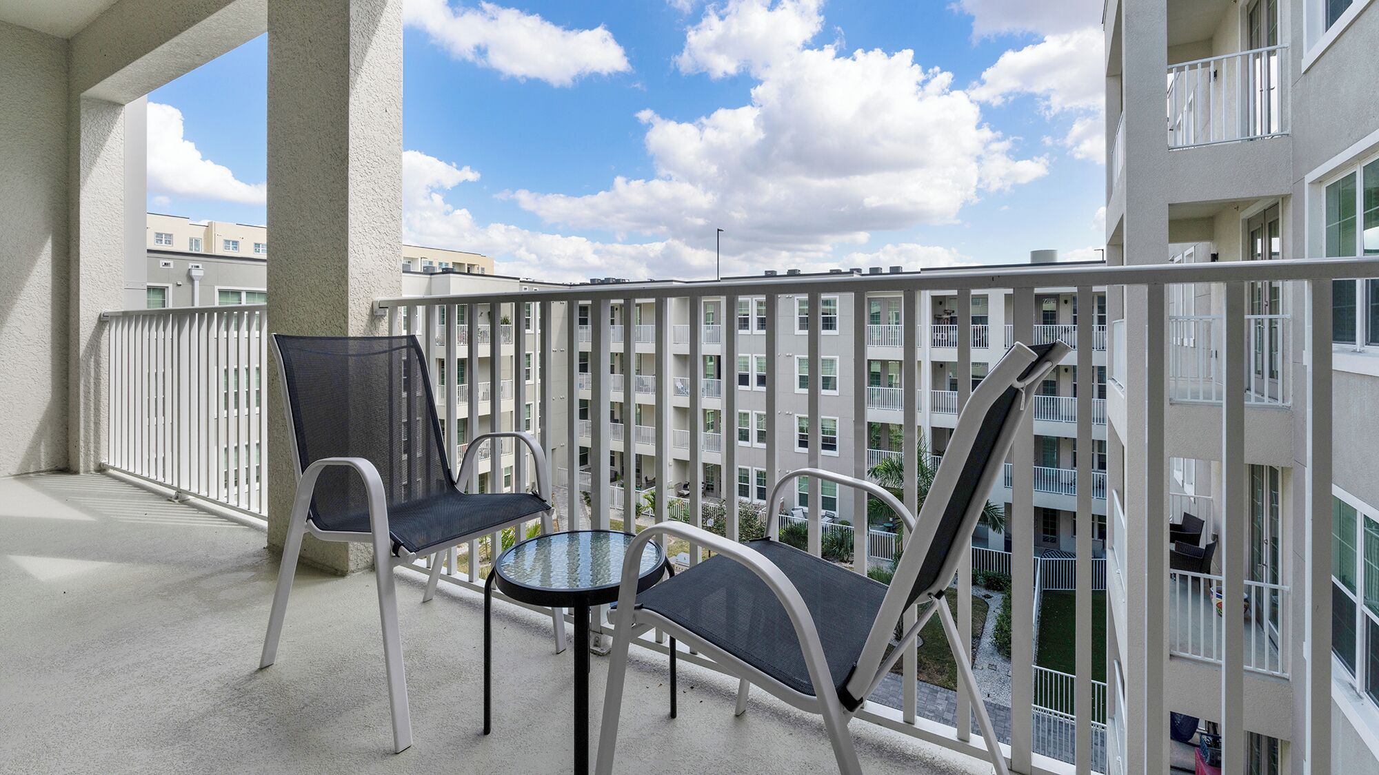 A balcony with two chairs and a small table, overlooking a residential building with multiple balconies.