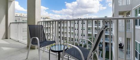 A balcony with two chairs and a small table, overlooking a residential building with multiple balconies.