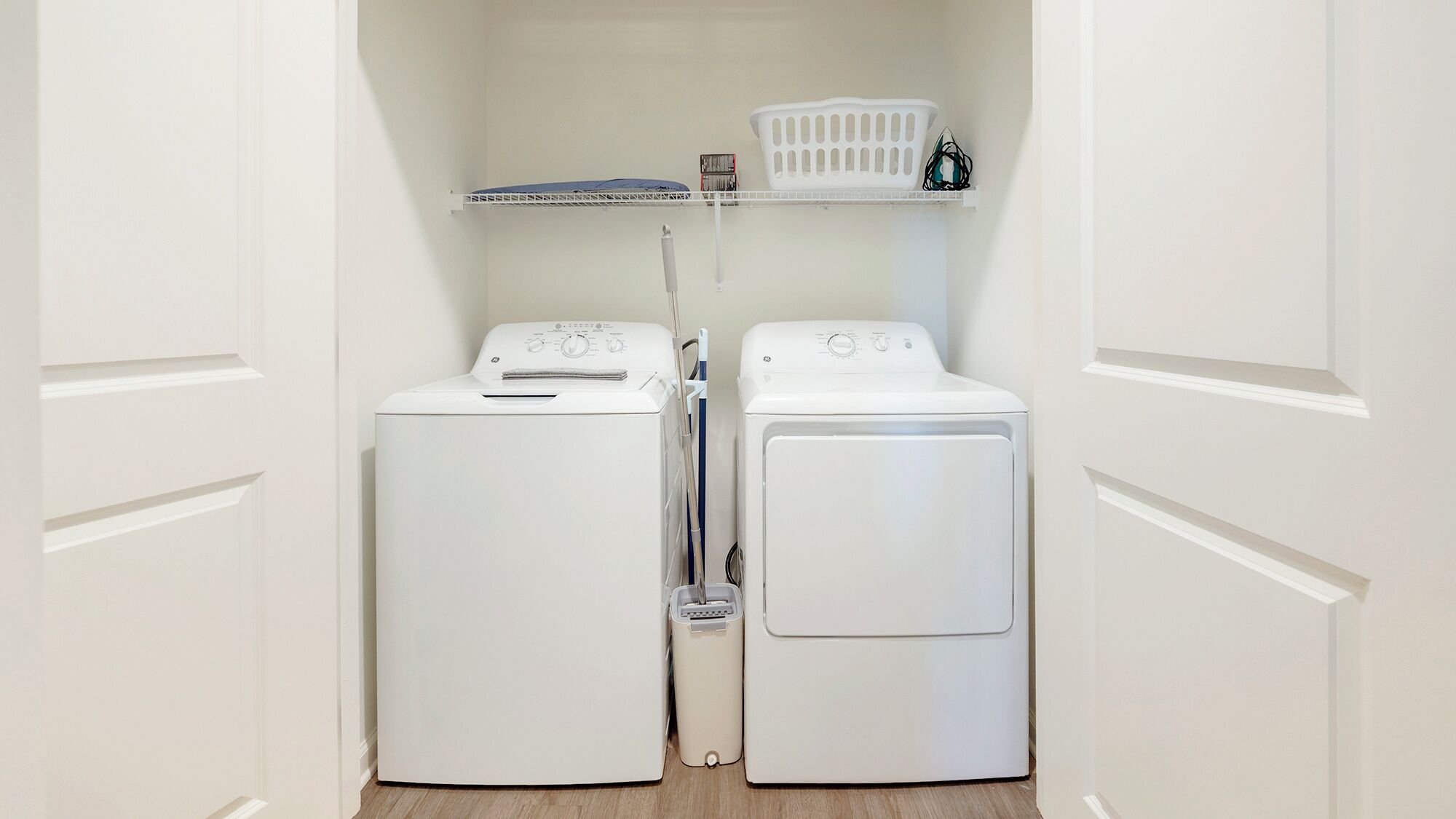 A laundry room with two white front-loading washing machines and a shelf above them.