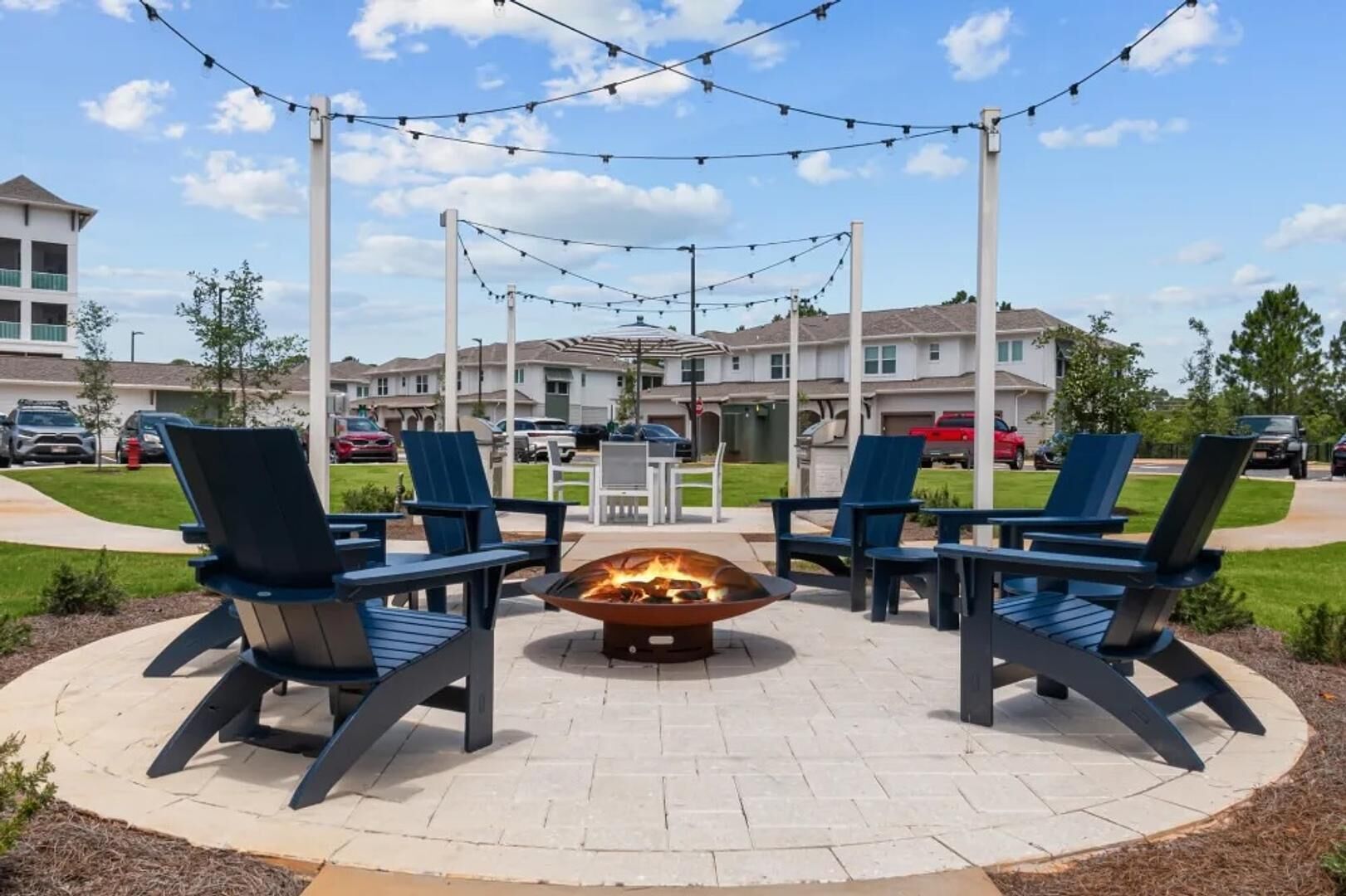 An outdoor seating area with a fire pit and chairs, surrounded by a paved patio.
