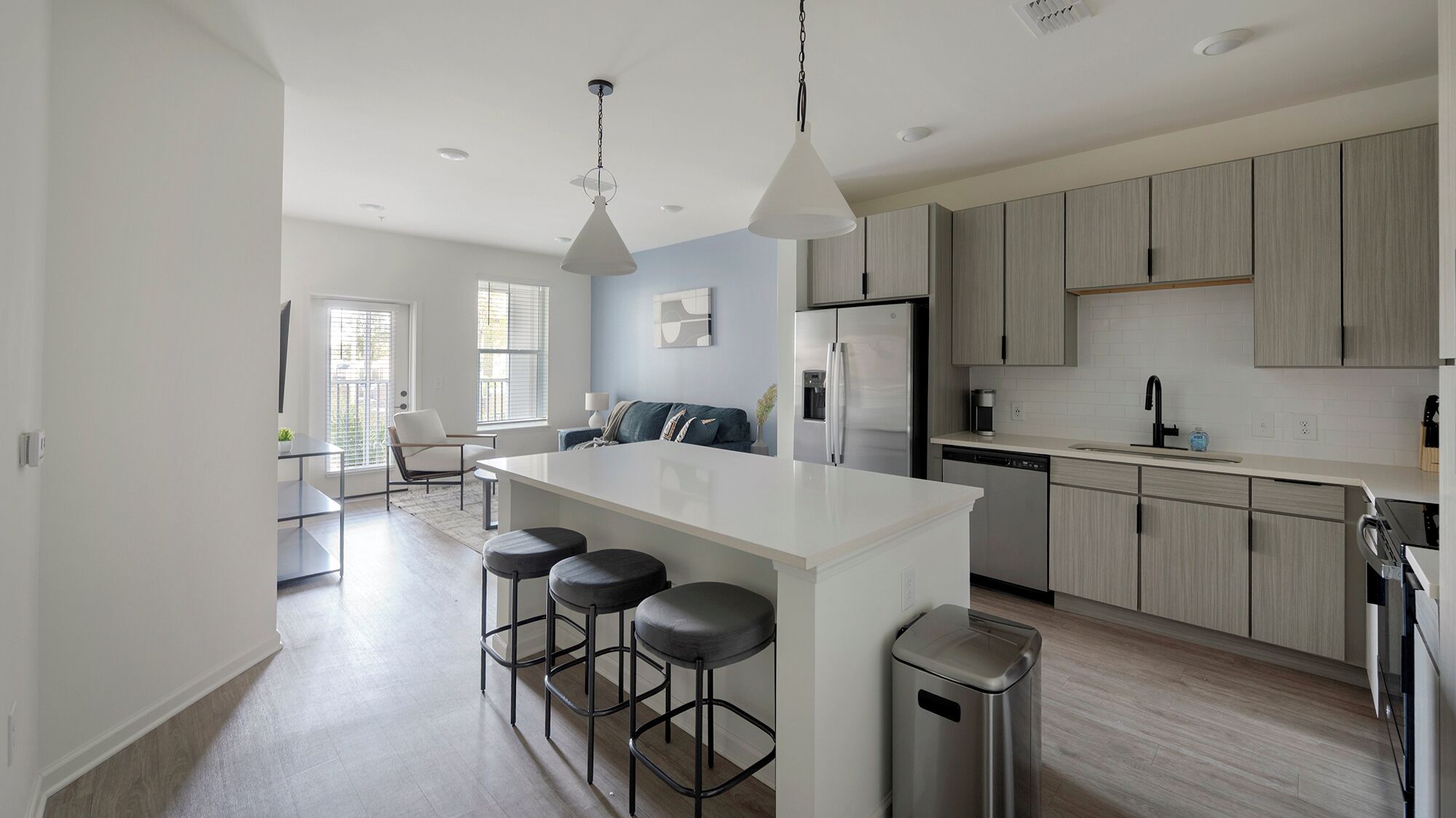 A modern kitchen with a central island, bar stools, stainless steel appliances, and light wood cabinetry.