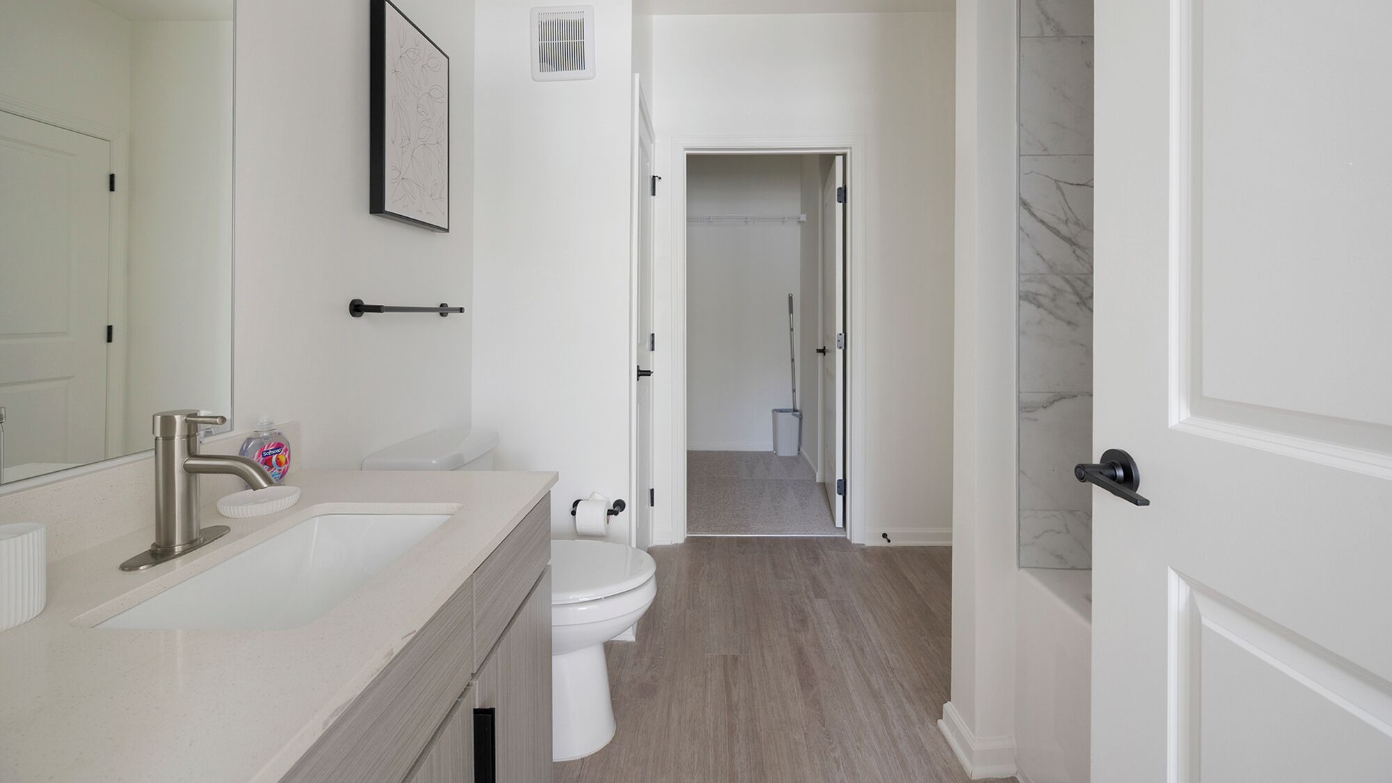 A modern bathroom with a sink, toilet, and a hallway leading to another room.