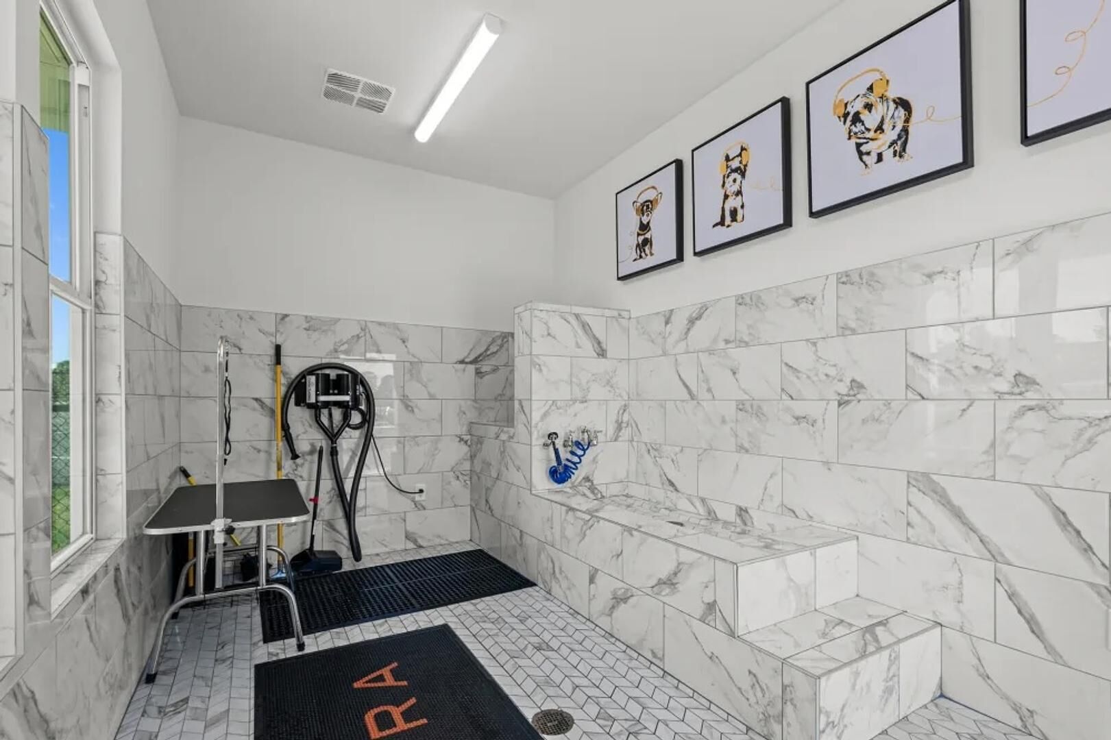 A modern bathroom with marble tiles, a shower area, and framed artwork on the wall.