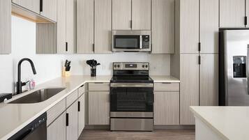 A modern kitchen with light wood cabinets, stainless steel appliances including a microwave, oven, and dishwasher, and a black faucet.