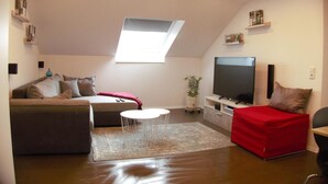 A modern living room with a sofa, a red ottoman, a TV, and a skylight. - Alb-Biosphere Holiday Apartment (Ingstetten)