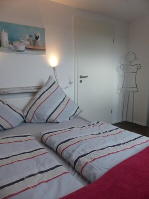 Una camera da letto con un letto, cuscini, un comodino, una lampada a parete e una porta.