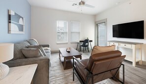A modern living room with a sofa, armchair, coffee table, and a TV mounted on the wall. - Landing Furnished Apartments - Rockport (Rockport)