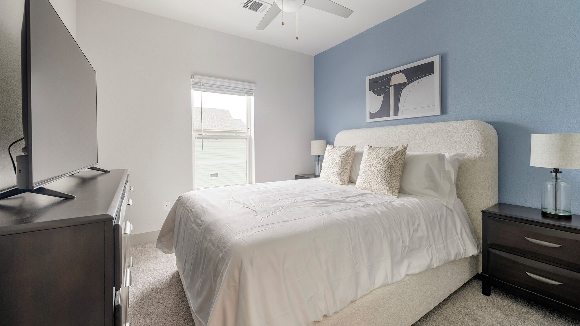 Un dormitorio con cama, escritorio, silla, ventana y ventilador de techo.