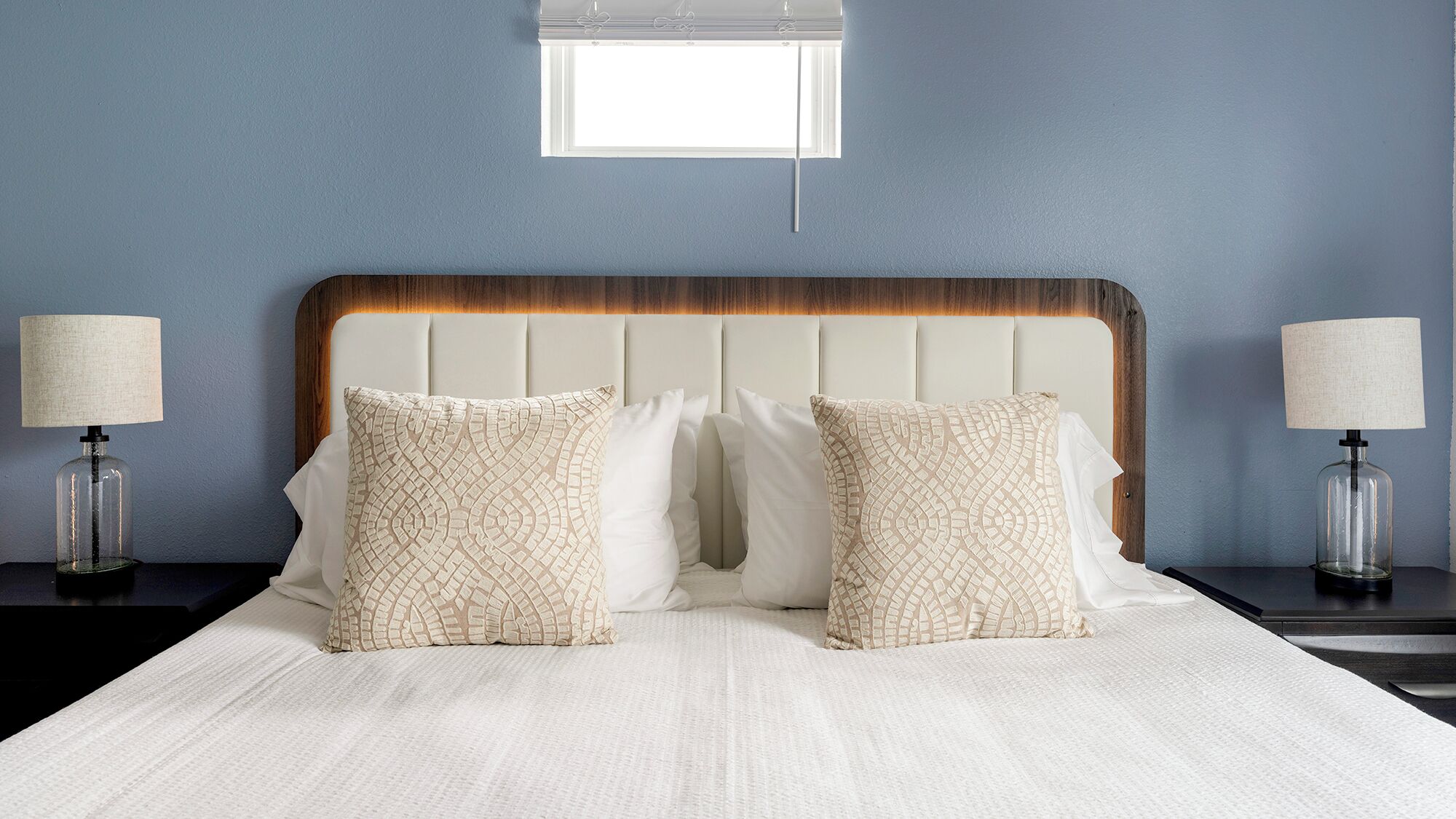 A neatly made bed with a wooden headboard, two bedside lamps, and a window above.
