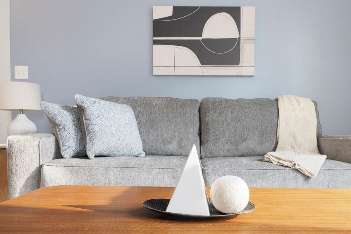 A modern living room with a grey sofa, patterned cushions, a white spherical object, and a lamp.