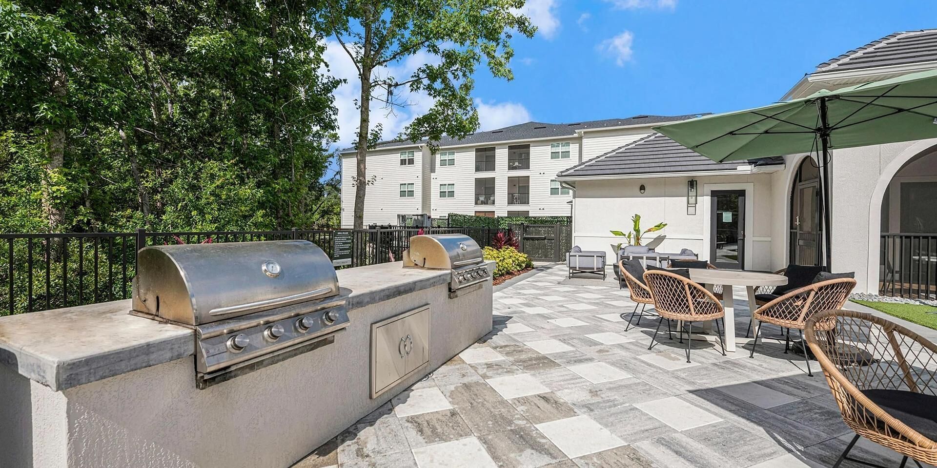 Eine Terrasse im Freien mit integriertem Grill, Korbstühlen und einem Tisch.