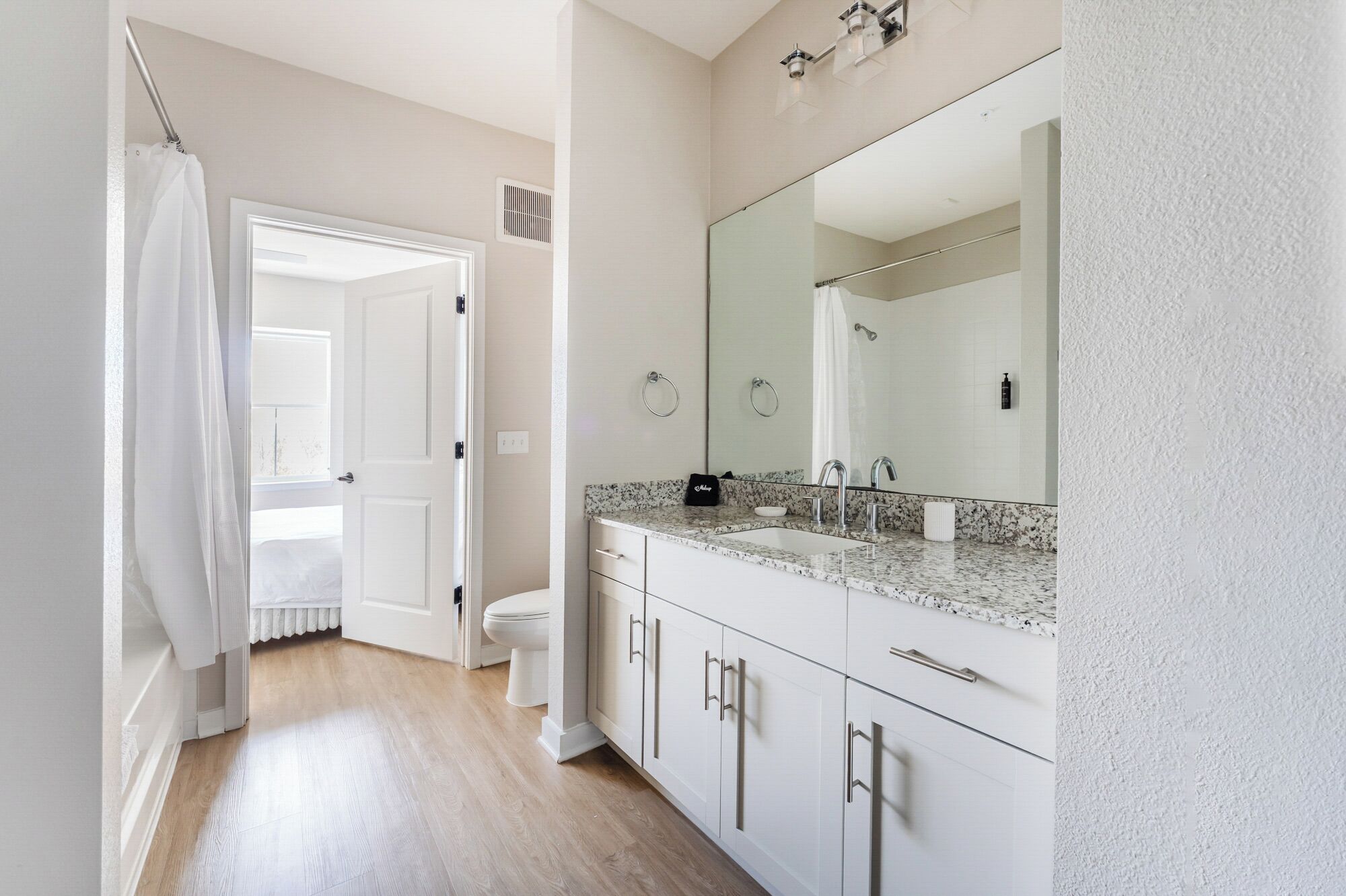 Een badkamer met een grote spiegel, witte kastjes, een wastafel en een toilet.