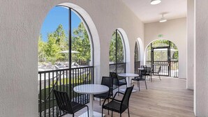 Un espace extérieur aménagé, abrité et doté de tables et de chaises rondes, de grandes fenêtres en arc de cercle, et offrant une vue sur une piscine et un espace verdoyant.